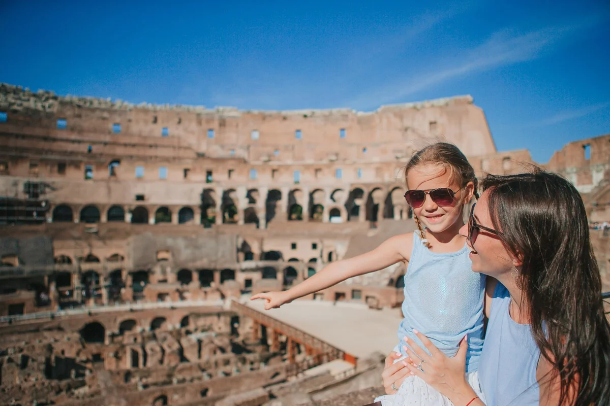 Mãe e filha sorrindo no interior do Coliseu em Roma com céu azul ao fundo