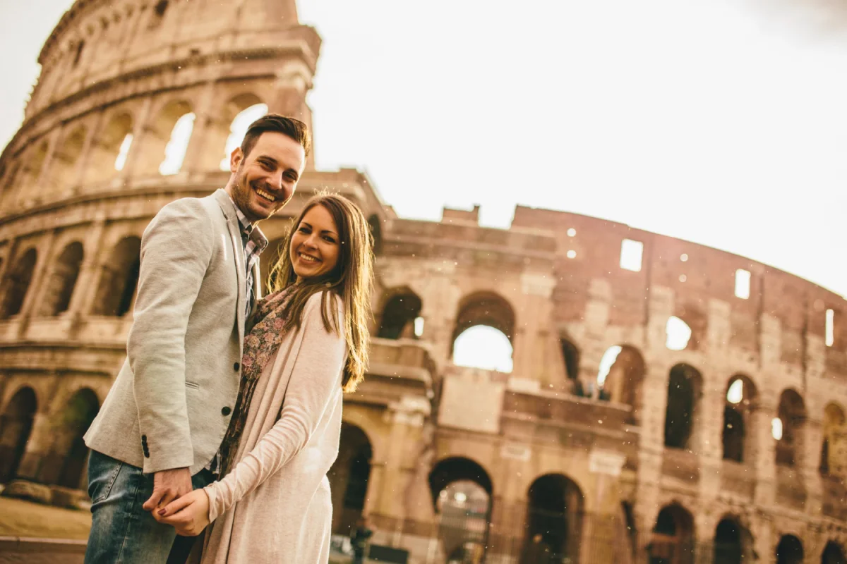 Casal sorridente de mãos dadas em frente ao Coliseu em Roma durante o dia