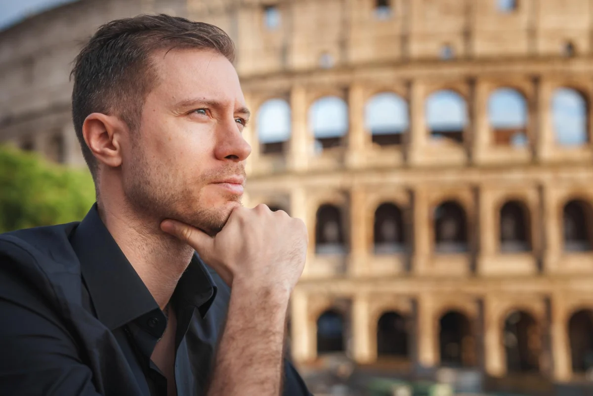 Homem pensativo com camisa preta em frente ao Coliseu em Roma