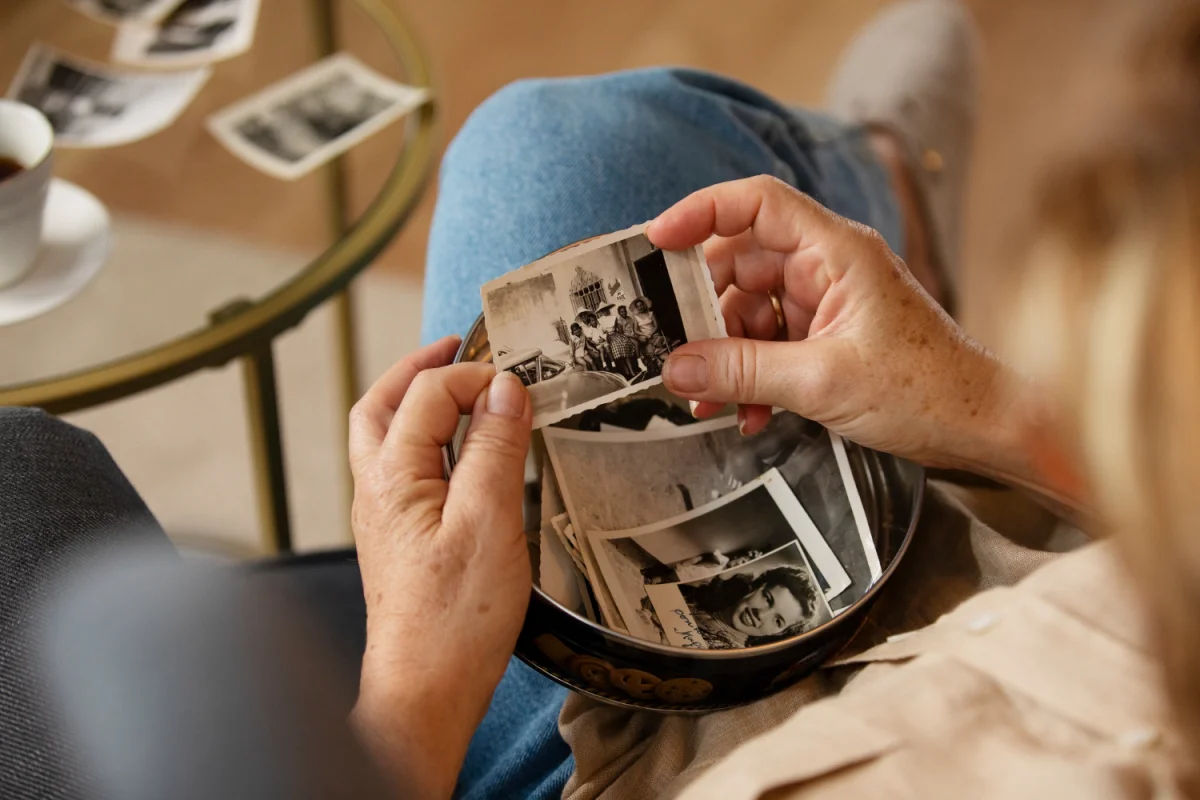 Pessoa segurando fotos antigas em preto e branco sentada com uma caixa de fotos no colo