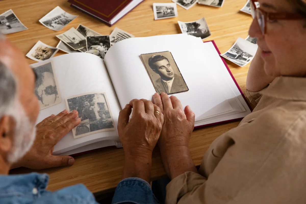 Casal idoso olhando álbum de fotos antigas com fotografias em preto e branco sobre mesa de madeira