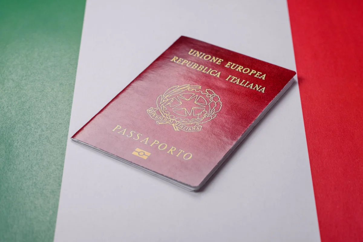 Passaporte italiano sobre a bandeira da Itália com as cores verde, branco e vermelho