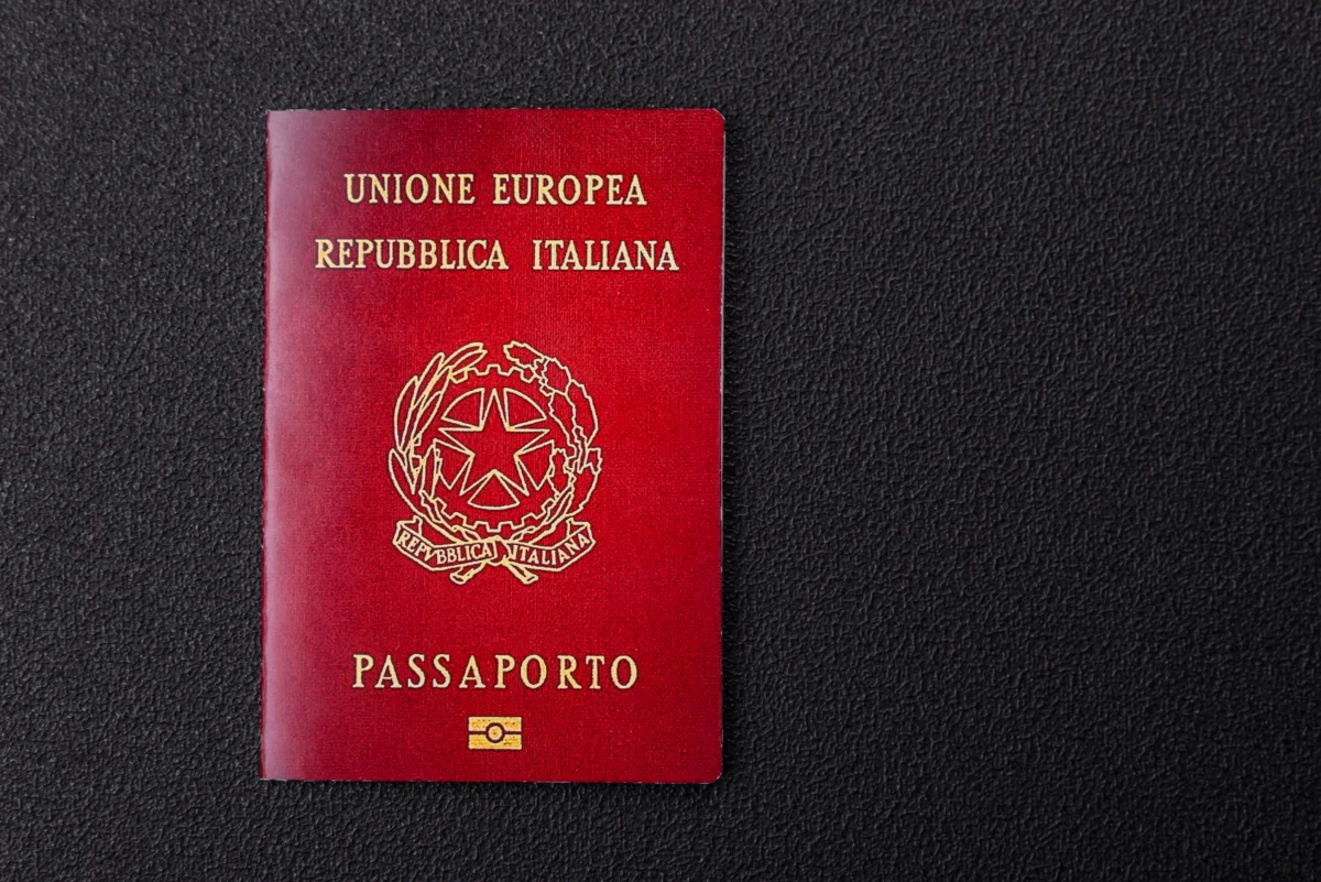 Passaporte italiano vermelho com texto em dourado sobre fundo preto texturizado